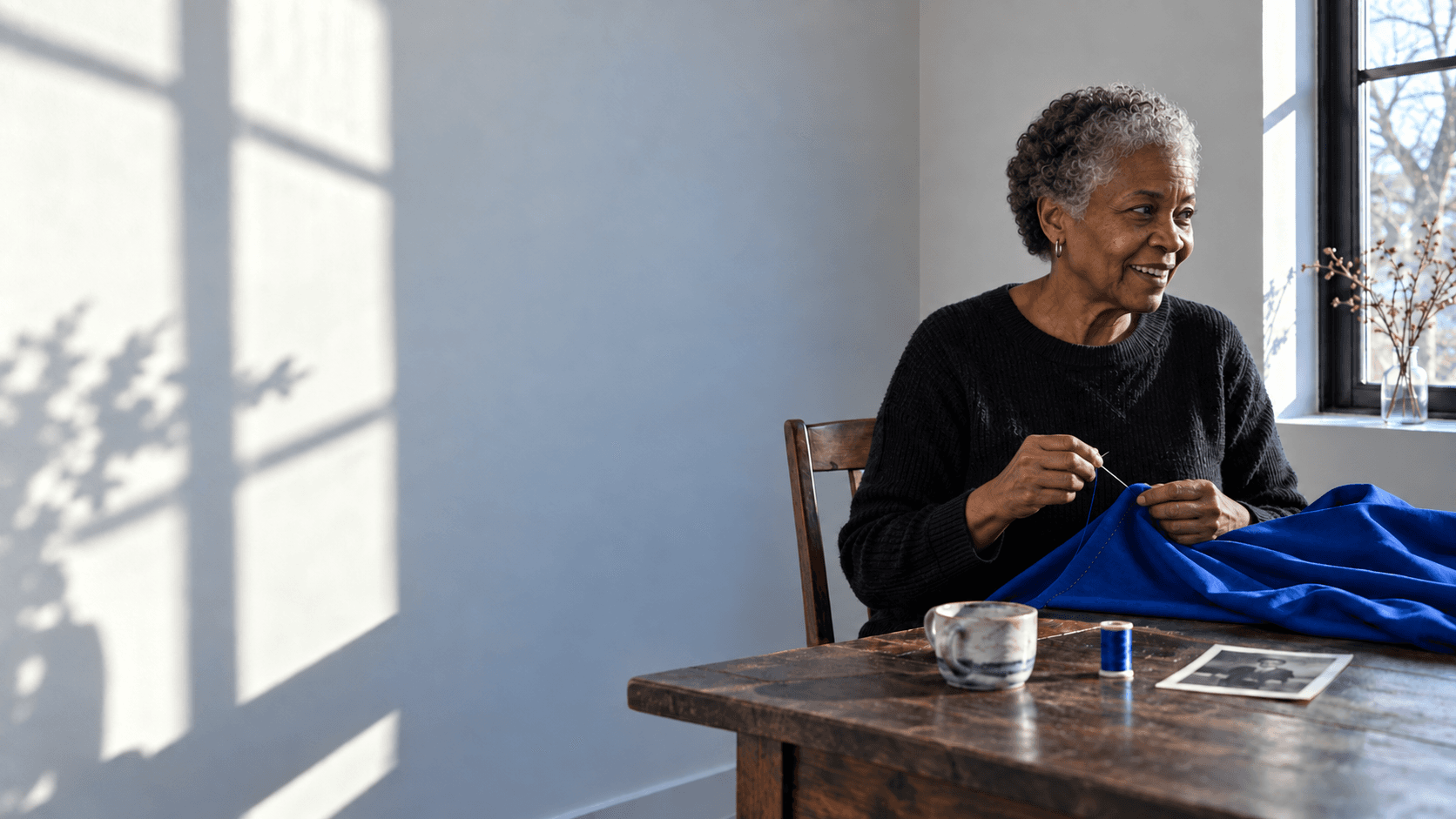 An older woman pausing her sewing to laugh with someone nearby